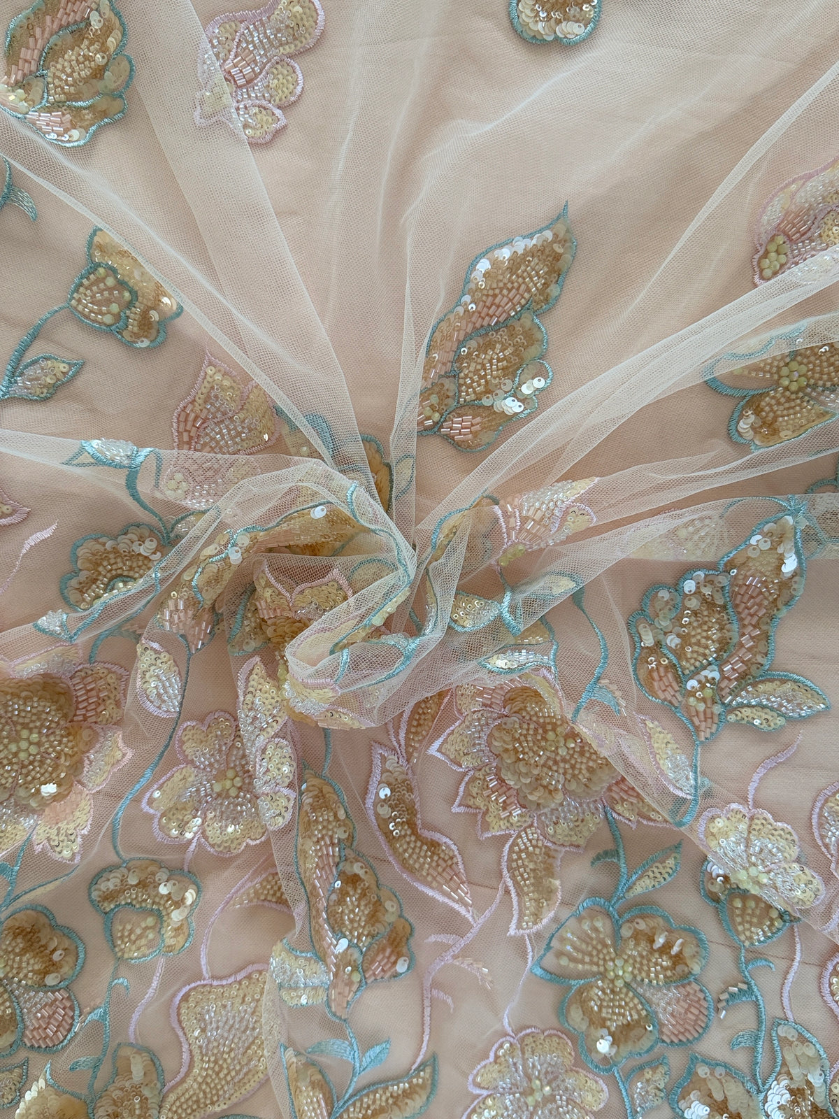 Close-up of embroidered fabric with gold and blue floral patterns on a beige background on Ruwa Sudanese toub