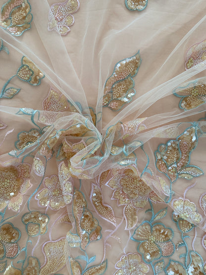 Close-up of embroidered fabric with gold and blue floral patterns on a beige background on Ruwa Sudanese toub